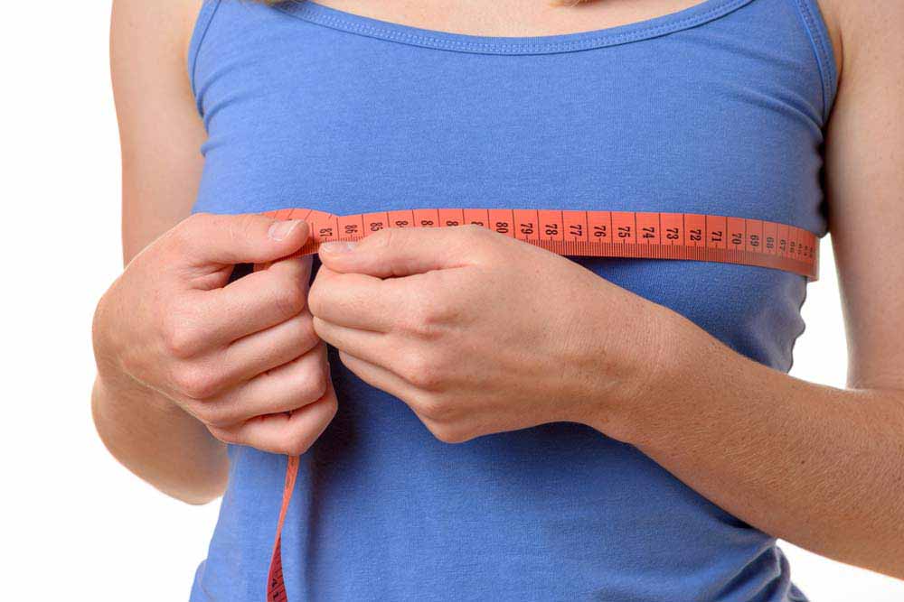 Young woman wearing summer t-shirt measuring her breasts with a tape measure