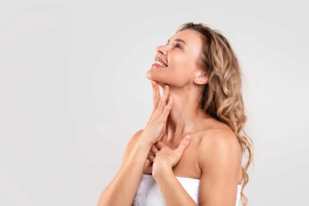 Woman wrapped in towel touching neck and smiling